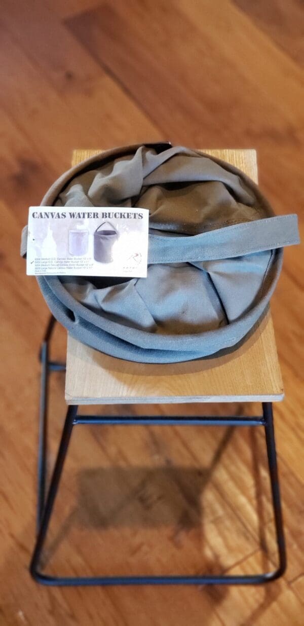 A Large Canvas Collapsible Water Bucket (ROTHCO) sits on a wooden table.