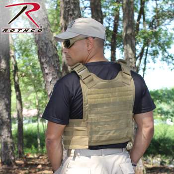 A man wearing a Rothco MOLLE Plate Carrier Vest (Multiple Pattern Choices) is standing in the woods.