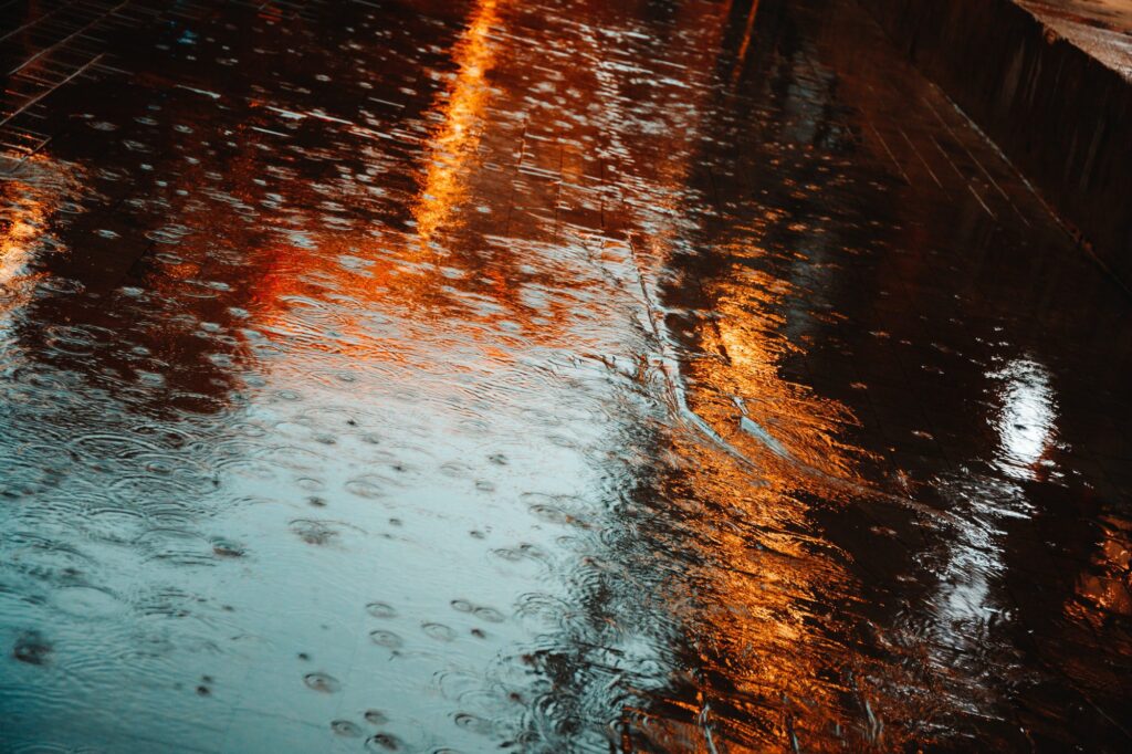 Abstract photography of rain. Raindrops on asphalt in the light of evening lights.