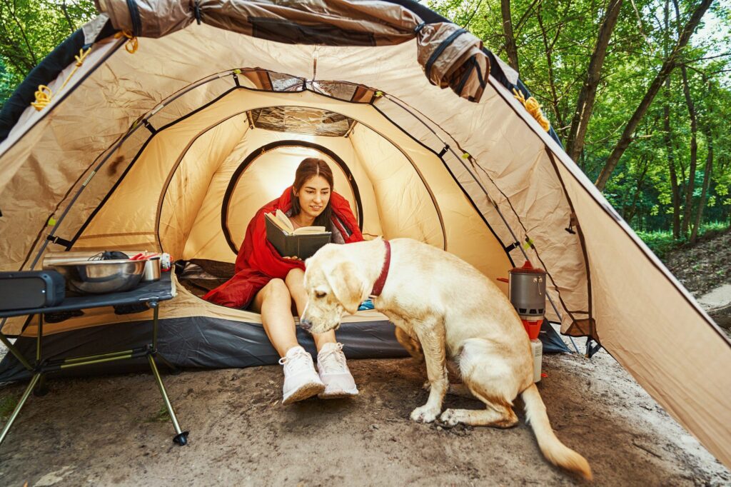 Cheerful woman with book and dog on camping