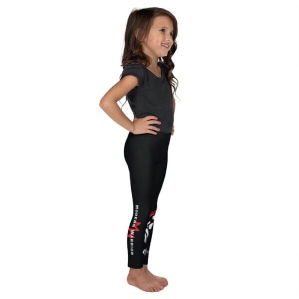 A little girl wearing black leggings adorned with a red heart showcasing MW Combatives Kid's Spats.
