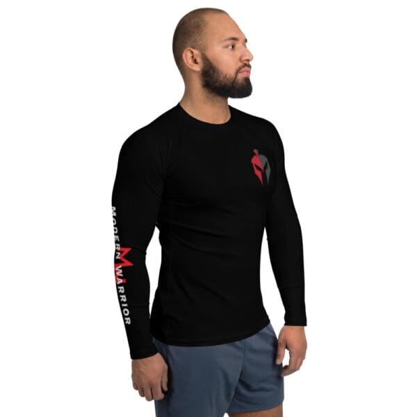 A man wears a MW Combatives Men's Rash Guard while sporting a black long-sleeved shirt with a red logo.