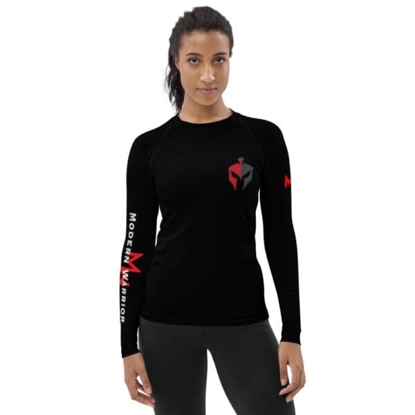 A woman wearing a black long-sleeved MW Combatives Women's Rash Guard with a red logo.