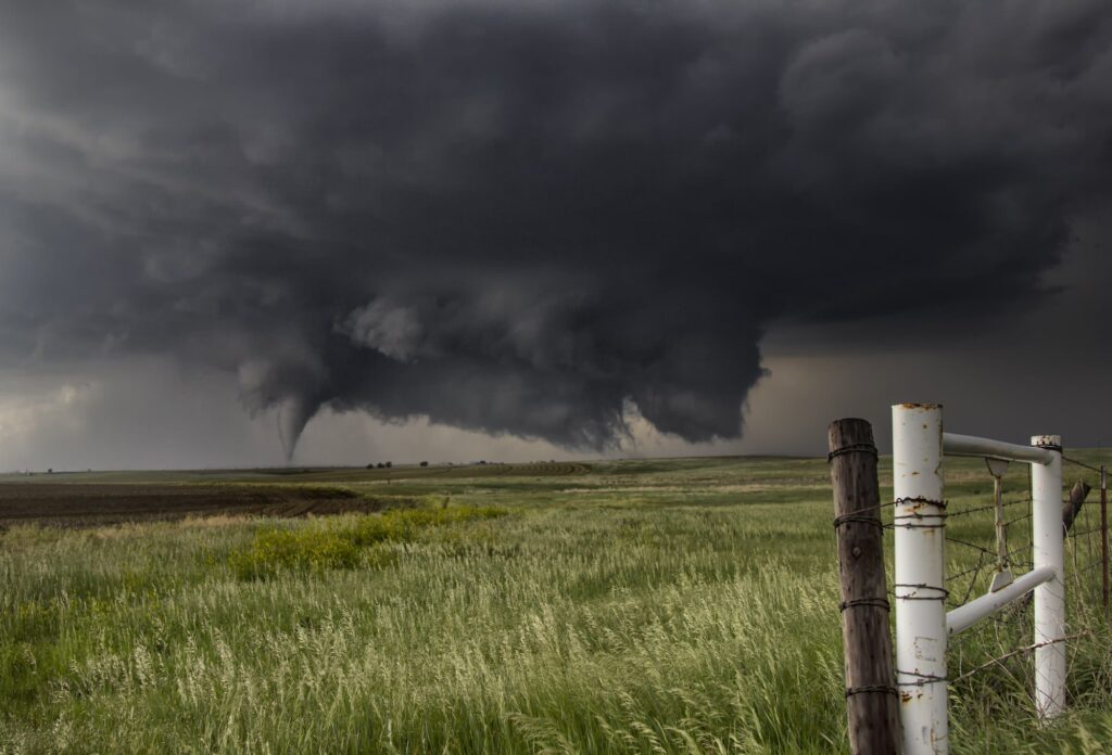 A large cone tornado touches down in an open country field from a very large angled ground-scraping