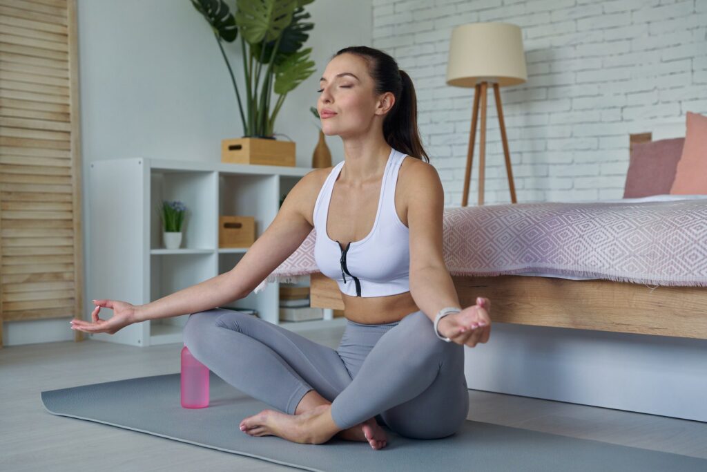 Attractive young woman in sports clothing meditating at home