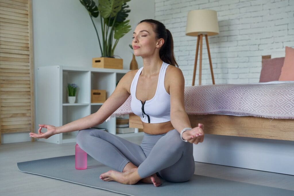 Attractive young woman in sports clothing meditating at home