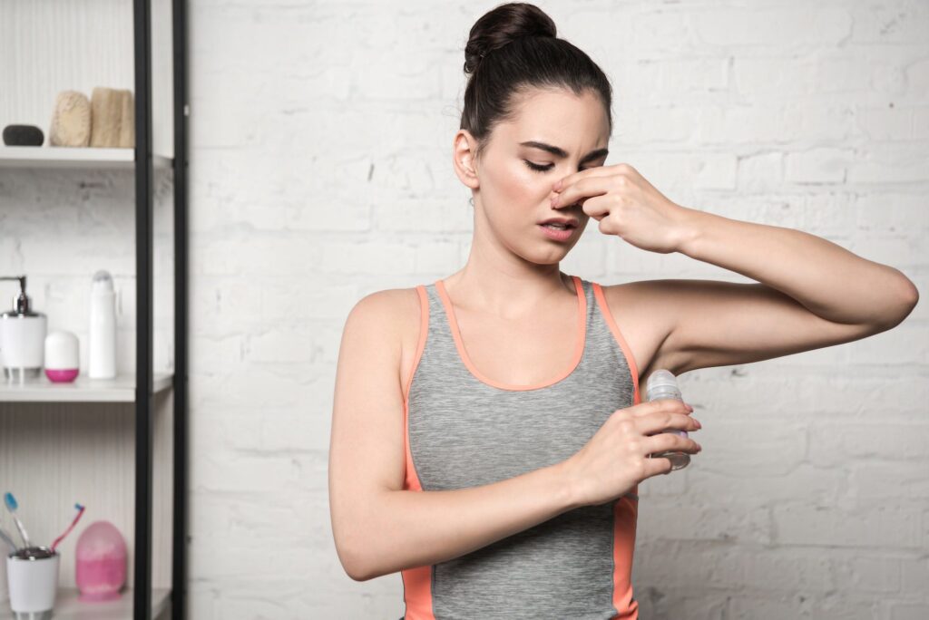 displeased woman plugging nose with hand while applying deodorant on underarm