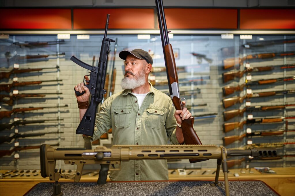Happy male hunter with two rifles in gun store