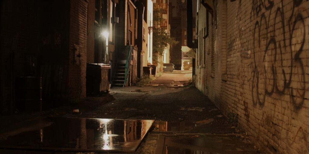 An alleyway at night with a puddle.
