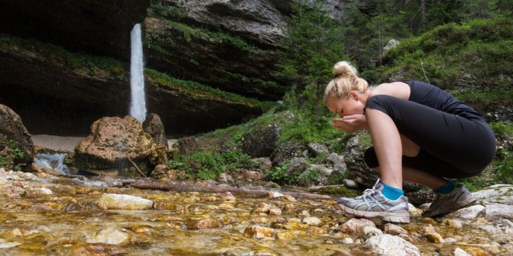 A woman crouching in front of a waterfall.