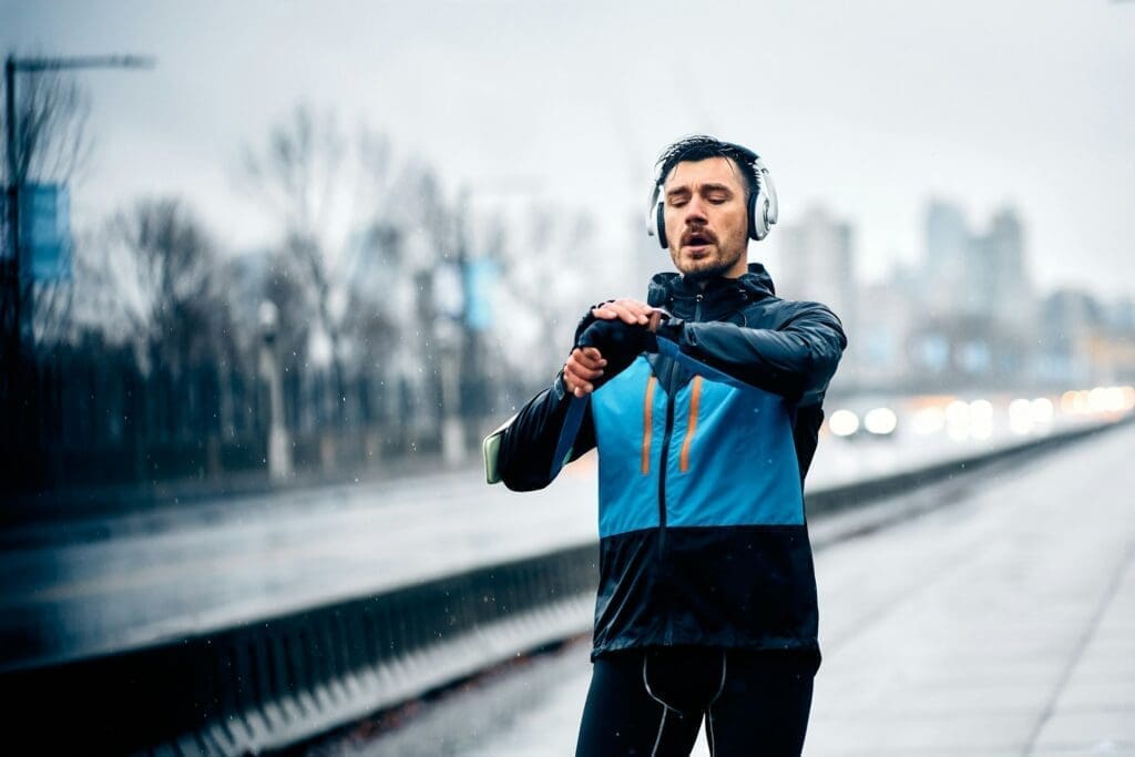 Male runner checking his fitness tracker after jogging in rain.