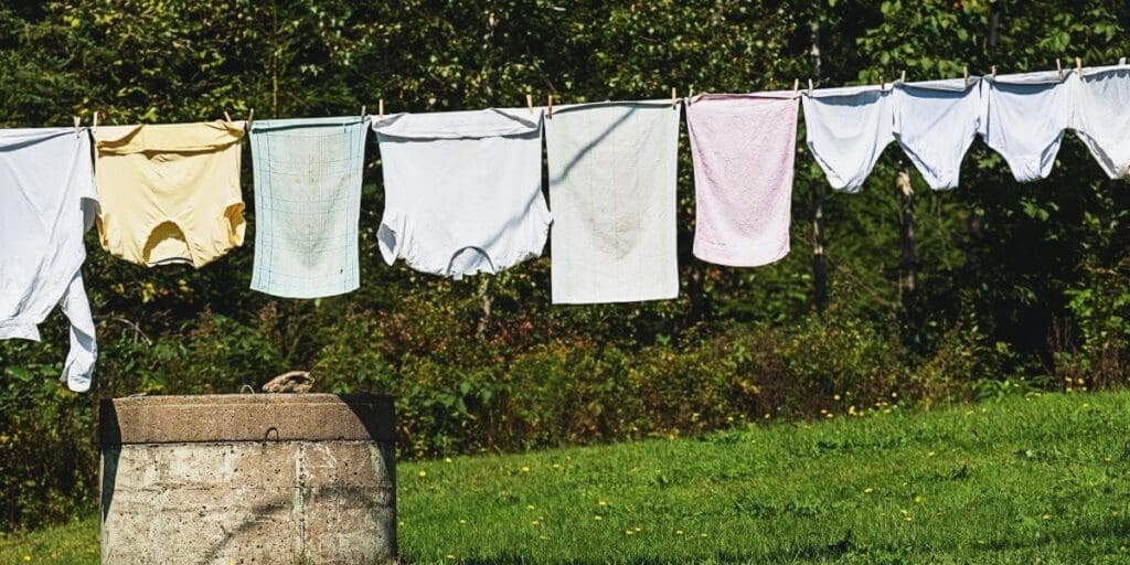 Laundry, hand-washed clothes hanging to dry on a clothesline outdoors with greenery in the background.