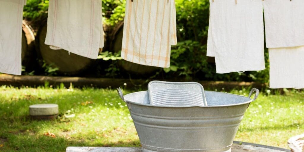 Clothes hanging to dry above a metal wash tub in a garden setting after being washed by hand.
