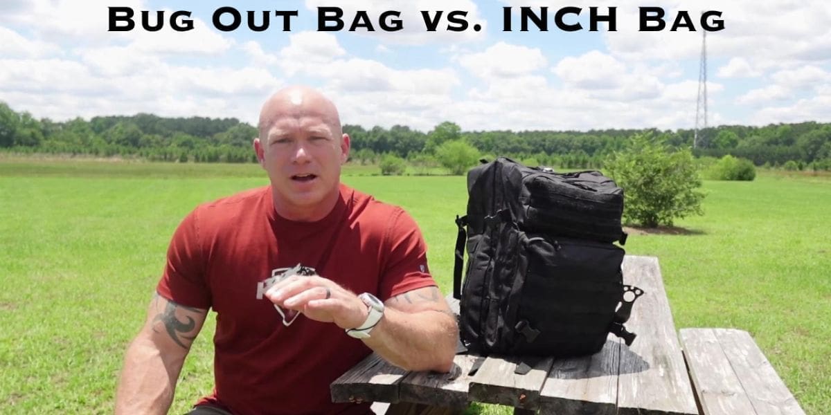 A person in a red shirt sits on a wooden picnic table next to a black backpack in an open field under a blue sky with clouds. Text above reads "Bug Out Bag vs. INCH Bag.