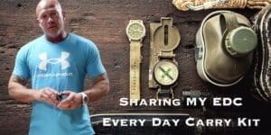 Man presenting his everyday carry items, including a watch and compass, displayed on a wooden background.