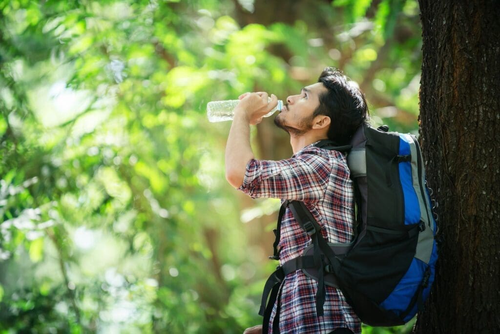 Young man thirsty and drink water during the trek behind a large tree.